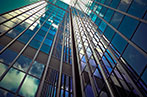 View of a glass office building from the ground up with the cloudy blue sky reflected on the surface